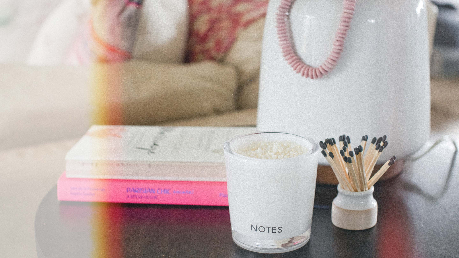 White scented candle decorating coffee table with books and matches