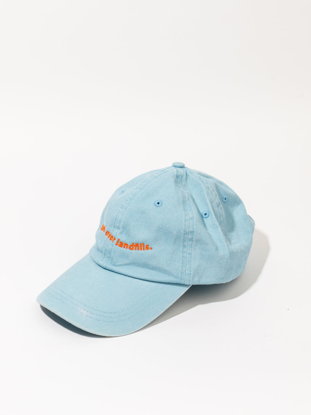 A light blue pigment dyed baseball cap with orange embroidery on the front panel, displayed on a white background.
